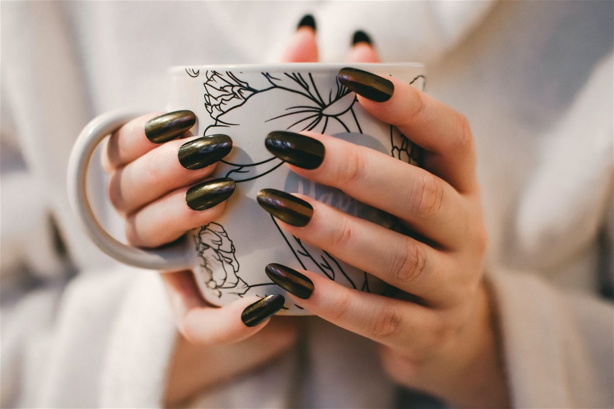 Hands holding a coffee cup, dark nail polish